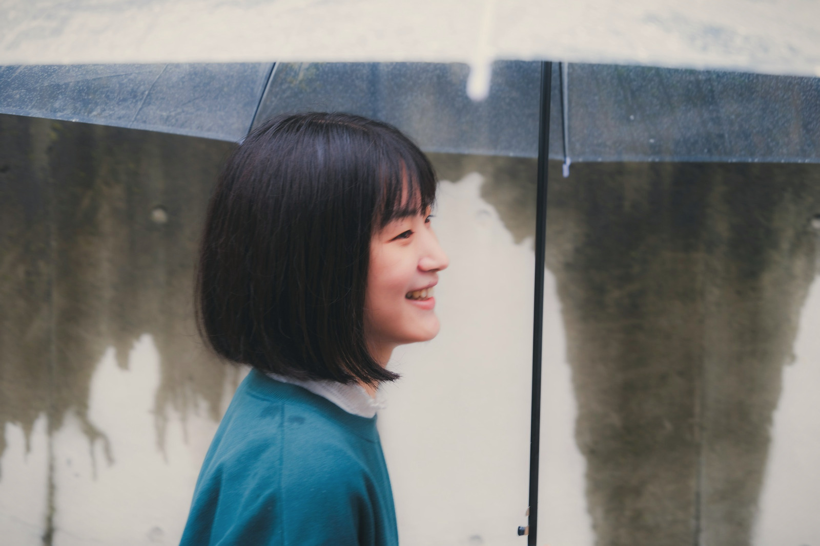 A young woman under a clear umbrella, smiling in the rain